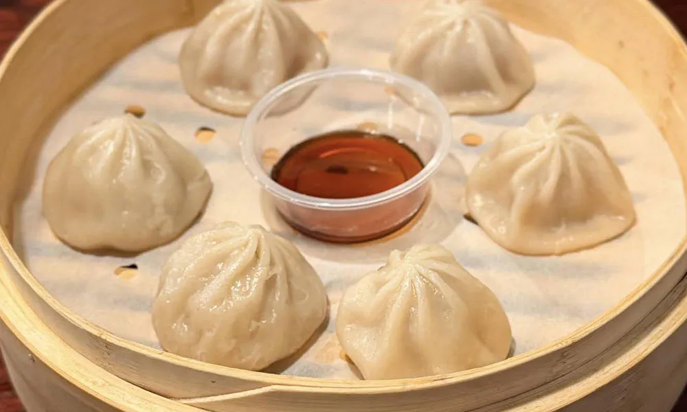 Steamed pork soup dumplings (xiaolongbao) in a bamboo steamer with soy sauce