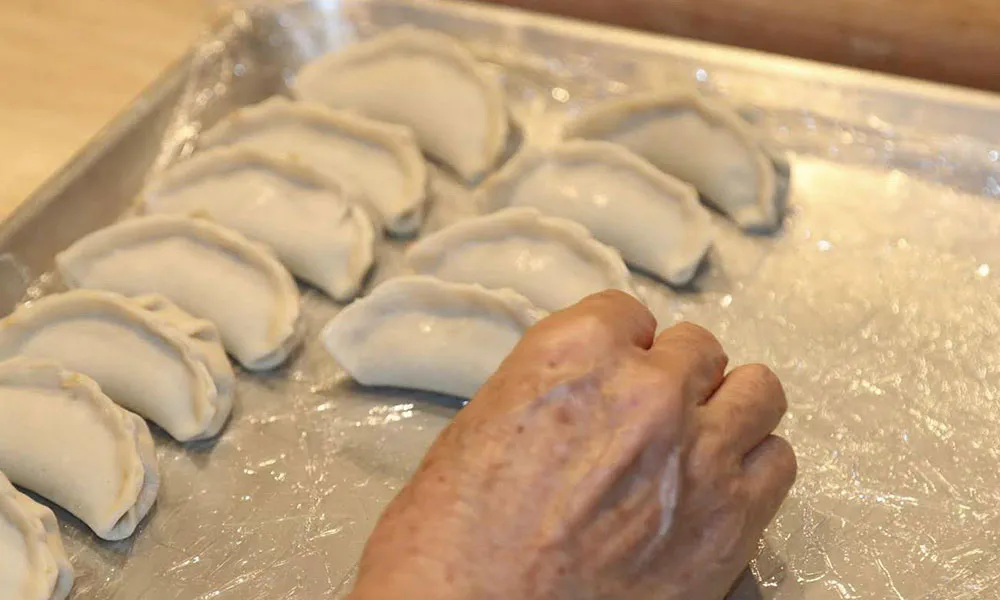 Hand-folded uncooked dumplings resting on a foil-lined baking tray