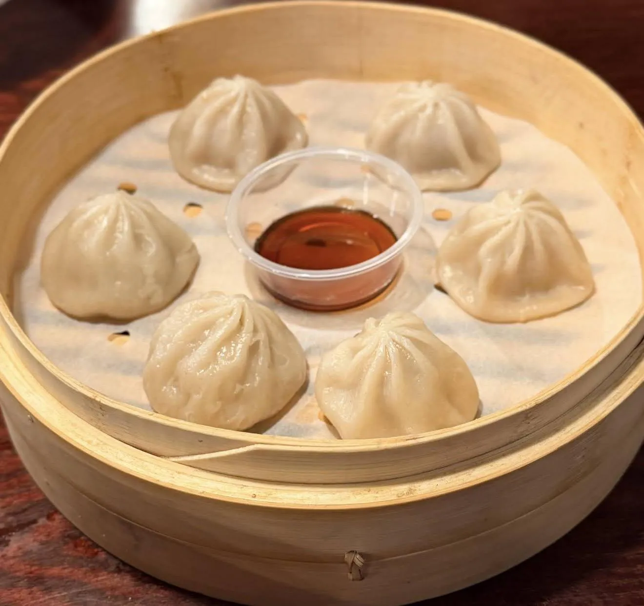Steamed pork soup dumplings (xiaolongbao) in a bamboo steamer with soy sauce